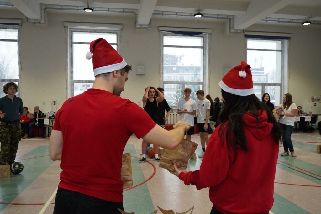 Nauczyciele wf-u w czapkach świętego Mikołaja rozdają nagrody podczas mikołajkowego turnieju koszykówki.