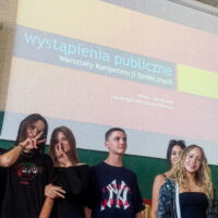 Grupa uczniów stojących na tle baneru z napisem "Wystąpienia publiczne".